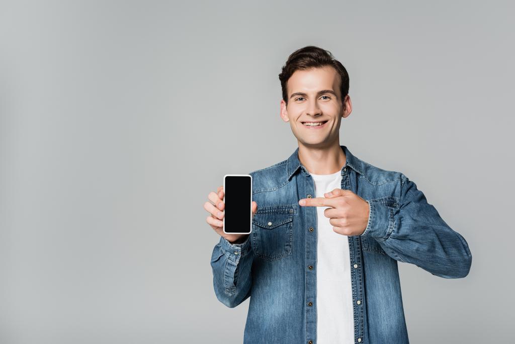 Uśmiechnięty mężczyzna wskazujący palcem na smartfona z pustym ekranem odizolowanym na szaro - Zdjęcie, obraz