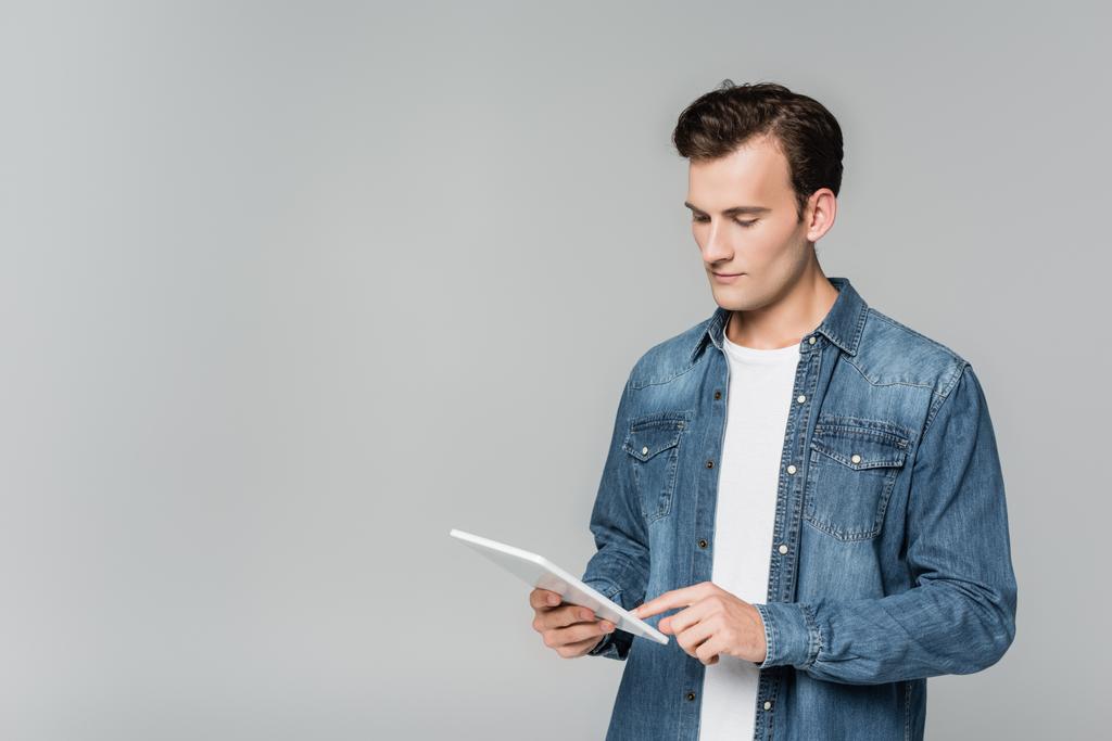 Młody mężczyzna w dżinsowej kurtce z cyfrowym tabletem odizolowanym na szaro - Zdjęcie, obraz