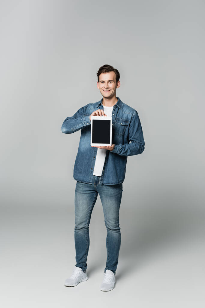 Mosolygós férfi farmerdzsekiben digitális tabletta üres képernyő szürke háttér - Fotó, kép