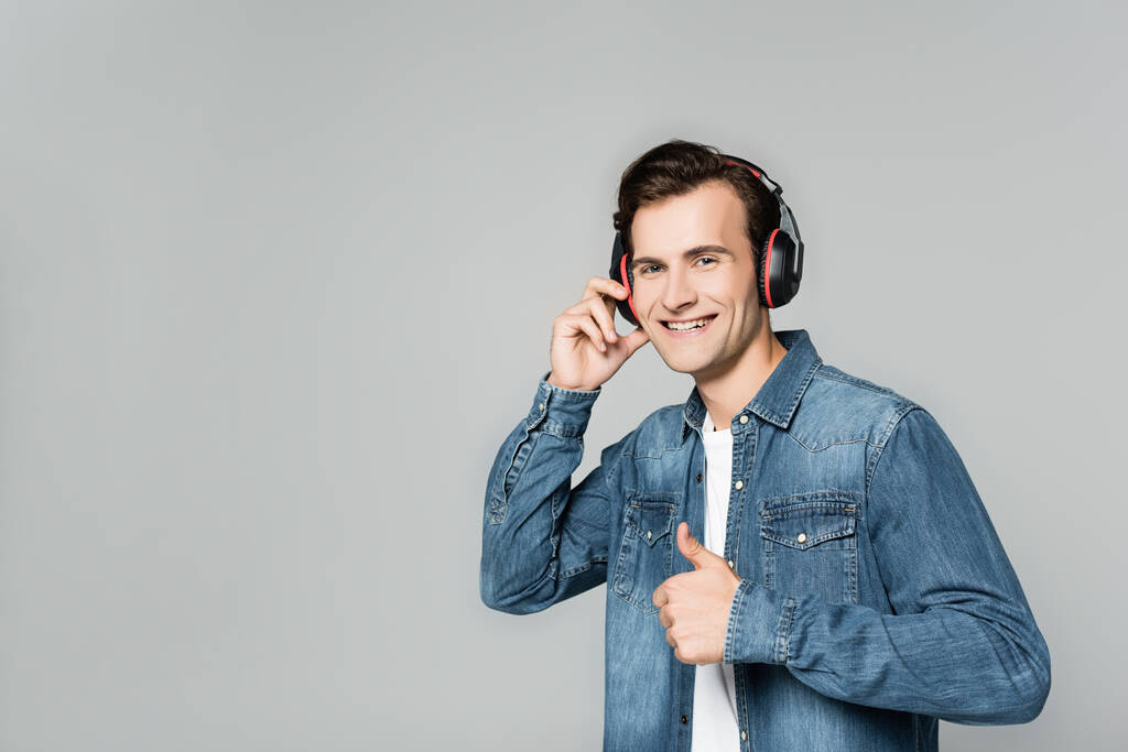 Homem alegre em fones de ouvido mostrando como gesto isolado em cinza - Foto, Imagem