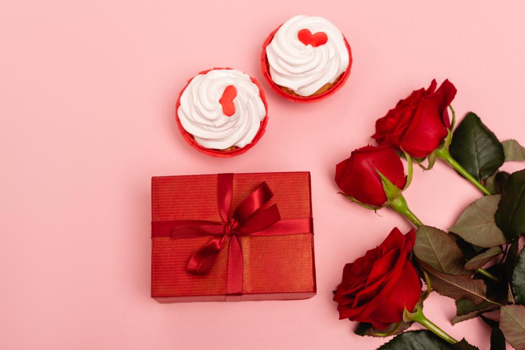 ピンクの背景に赤いバラとカップケーキの上からの眺め - 写真・画像