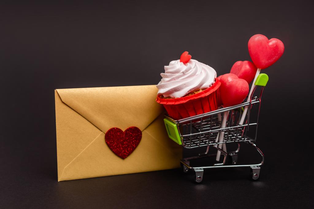 panier avec cupcake aux valentines et sucettes et enveloppe isolée sur noir - Photo, image