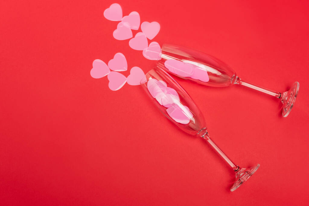 bovenaanzicht van roze hartjes in champagneglazen op rode achtergrond - Foto, afbeelding