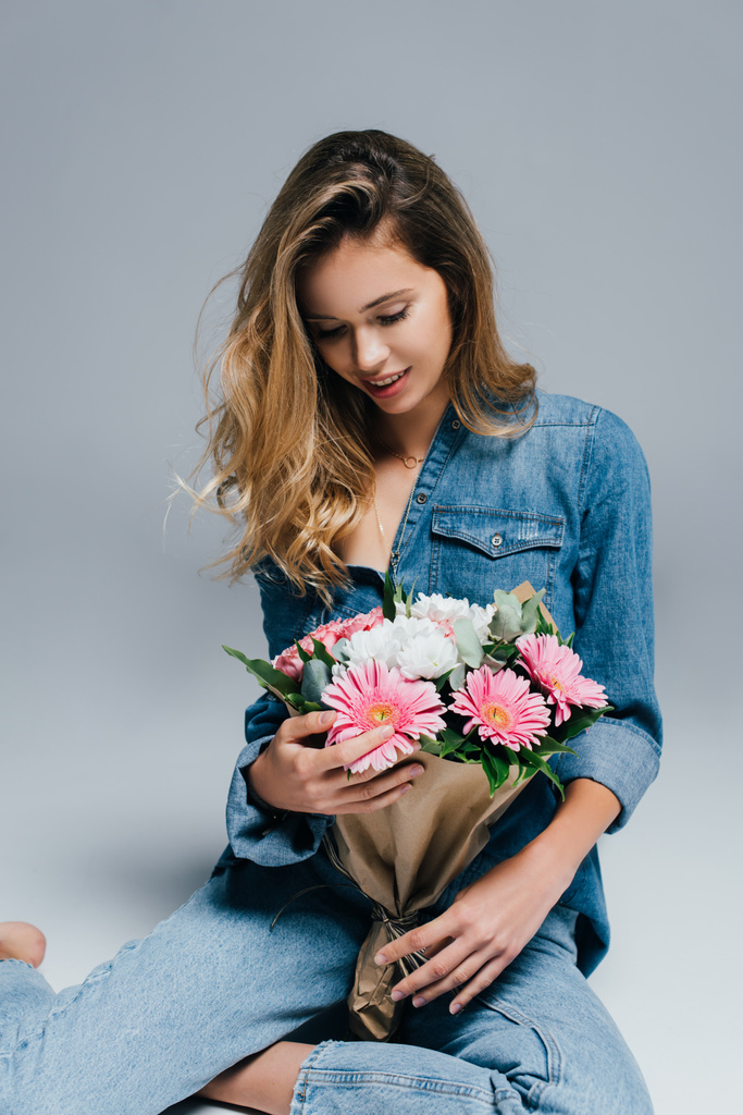 jeune, charmante femme en denim assis sur gris avec bouquet - Photo, image