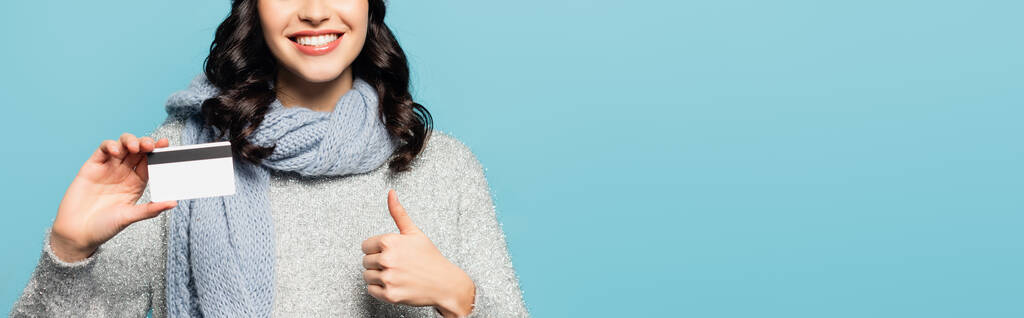 Cropped view of brunette woman wearing scarf showing thumb up while holding credit card isolated on blue, banner - Photo, Image