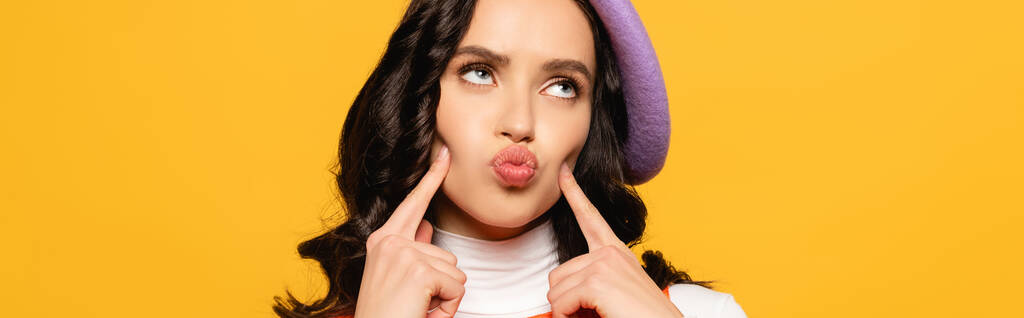 Brunette woman in beret with pouting lips looking up isolated on yellow, banner - Photo, Image