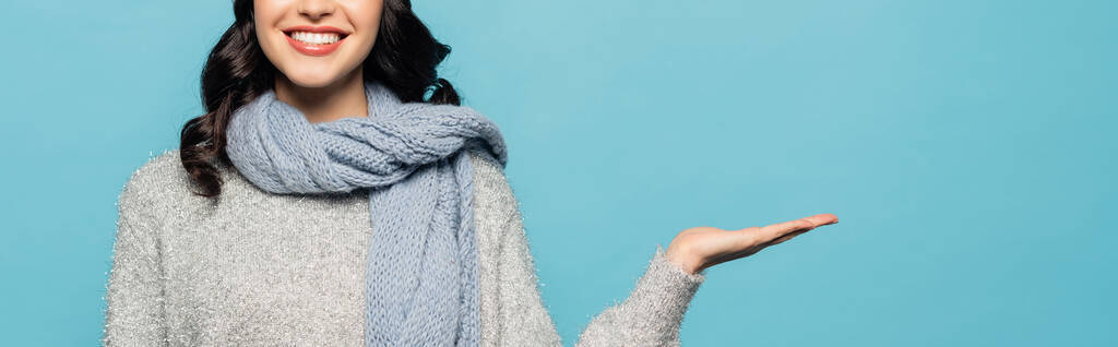 Обрізаний вид брюнетки жінки в шарфі, спрямований рукою ізольовано на синьому, банер
 - Фото, зображення
