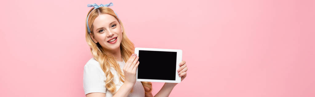 Lächelnde blonde junge Frau zeigt digitales Tablet isoliert auf rosa Banner - Foto, Bild