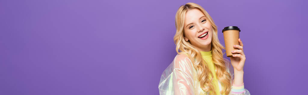 jovem loira feliz em roupa colorida com copo de papel isolado em roxo, banner - Foto, Imagem