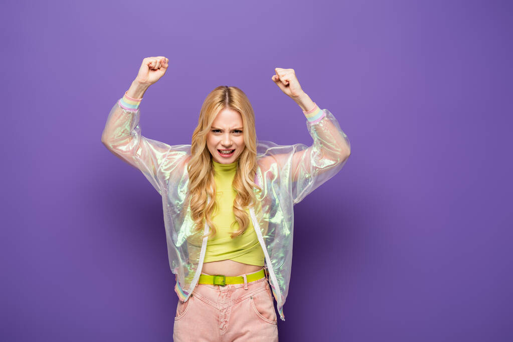 блондинка в красочном наряде с поднятыми кулаками на фиолетовом фоне - Фото, изображение