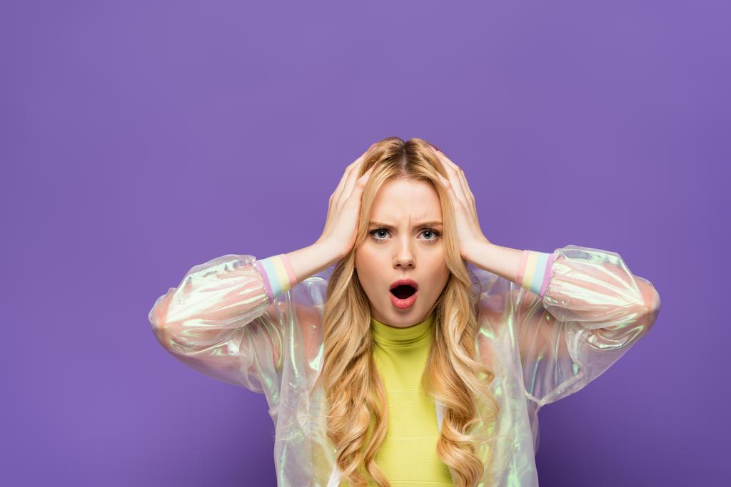 šokované blondýny mladá žena v barevné oblečení držení hlavy na fialovém pozadí - Fotografie, Obrázek