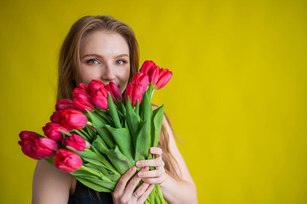 Kobieta z bukietem czerwonych tulipanów na żółtym tle. Szczęśliwa dziewczyna w czarnej sukience posiada mnóstwo kwiatów. Prezent na Walentynki. Najbardziej romantyczny dzień w roku.. - Zdjęcie, obraz