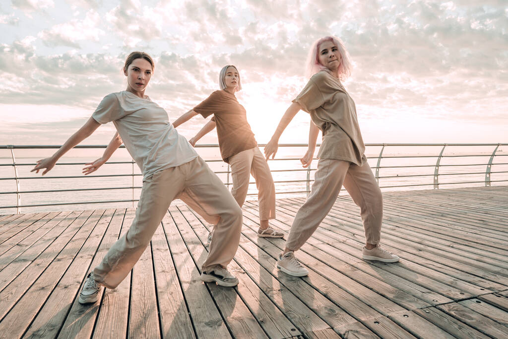 Jóvenes bailarinas adolescentes disfrutando de movimientos funky hip-hop. Mujeres modernas bailando estilo libre juntas en el dique de mar al amanecer. - Foto, Imagen
