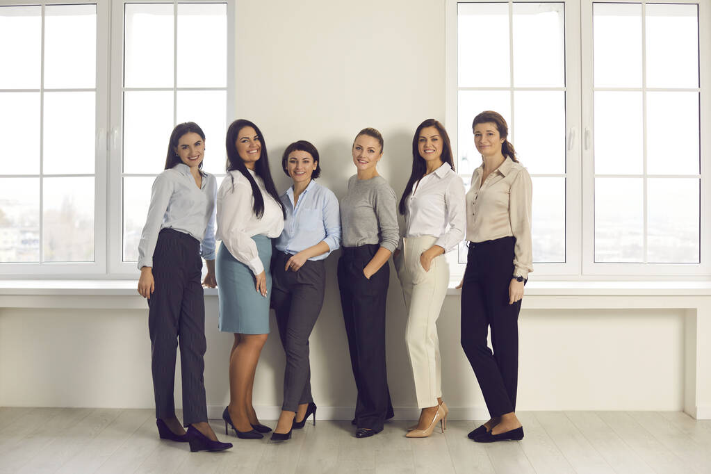 Équipe de femmes d'affaires heureuses debout ensemble dans un nouveau bureau et souriant à la caméra - Photo, image