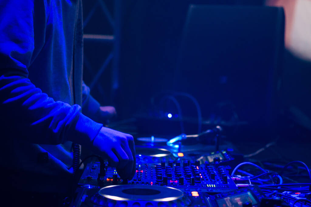 DJはナイトクラブで音楽を演奏する。青い色、ミキシングコントローラー、ディージェイの手 - 写真・画像