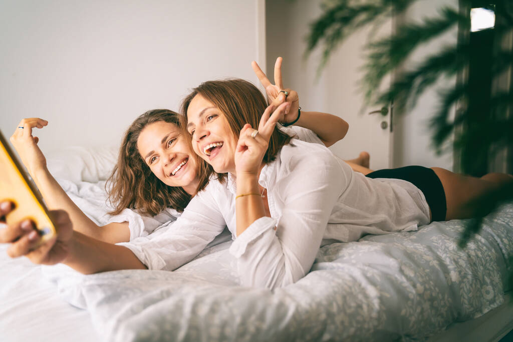 Молода красива весела лесбіянка закохана у те, що робить селфі на смартфоні вдома на ліжку
 - Фото, зображення