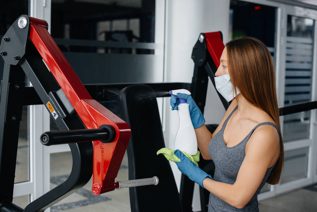 The girl in the mask disinfecting the gym equipment during a pandemic. - Photo, Image