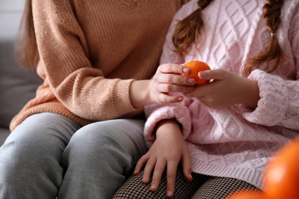 Mädchen mit frischer Mandarine sitzen drinnen auf dem Sofa, Nahaufnahme - Foto, Bild