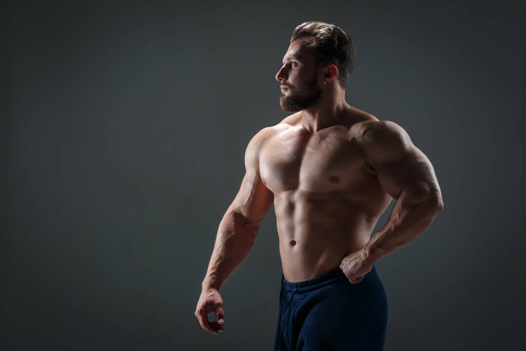 Mutiger athletischer Typ mit nacktem Oberkörper im Gegenlicht vor dunklem Hintergrund. - Foto, Bild