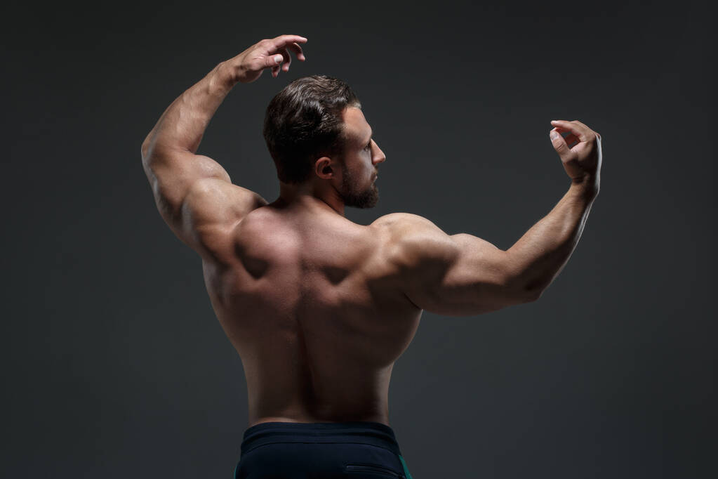 Portret van een jonge atletische man met een naakte romp met spieren geïsoleerd op een donkergrijze achtergrond, zicht vanaf de rug. - Foto, afbeelding