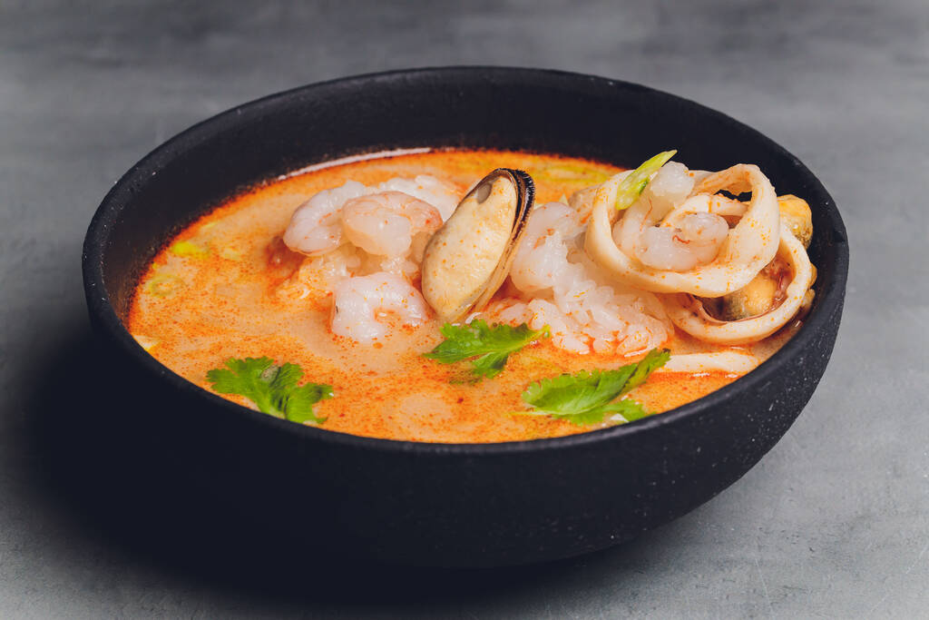Baharatlı Tayland çorbası Tom Yam, hindistan cevizi sütü, acı biber ve deniz mahsulü karides ve somon ile siyah arka planda. Asya mutfağı, restoran menüsü. - Fotoğraf, Görsel