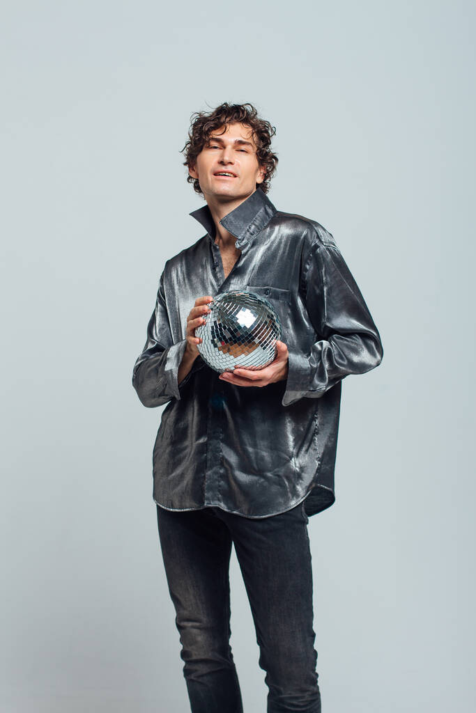Portrait de grand homme attrayant avec une boule de disco miroir sur un fond blanc. Beau homme posant avec une boule disco brillante en studio. - Photo, image