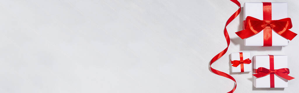Banner festivo en venta con cajas de regalo blancas con cinta de seda roja a la luz del sol con sombra en tablero de madera blanca, vista superior. - Foto, imagen