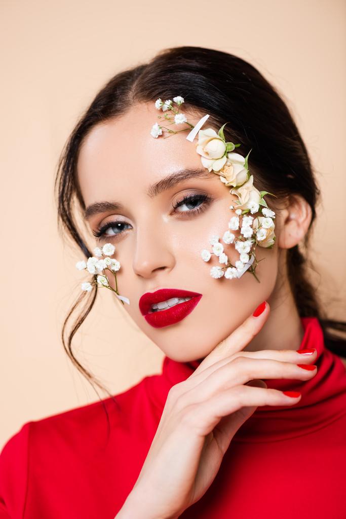 Kırmızı dudaklı ve yüzünde çiçekler olan genç bir kadın pembe kameraya bakıyor.  - Fotoğraf, Görsel