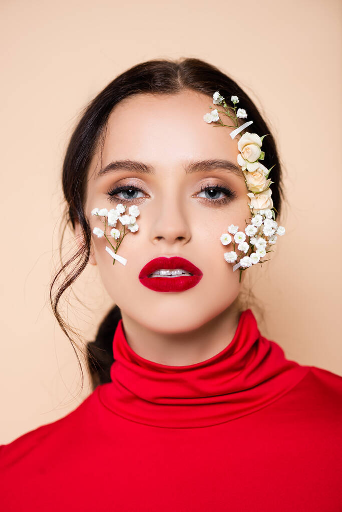 brunette woman with red lips and flowers on face looking at camera isolated on pink  - Photo, Image