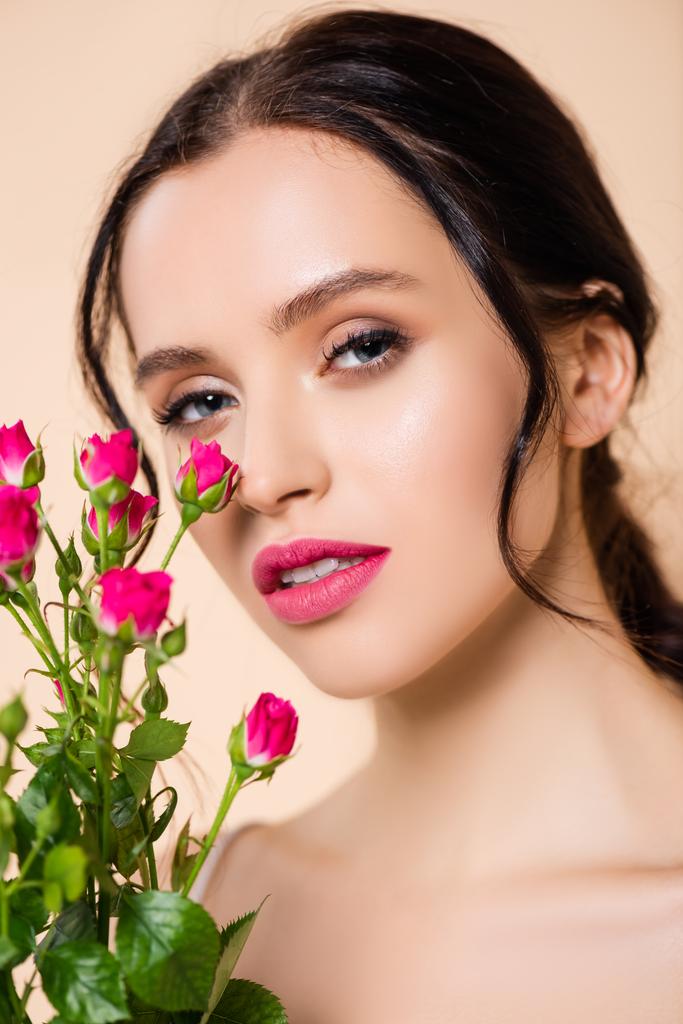 jeune femme regardant caméra près de fleurs isolées sur rose  - Photo, image
