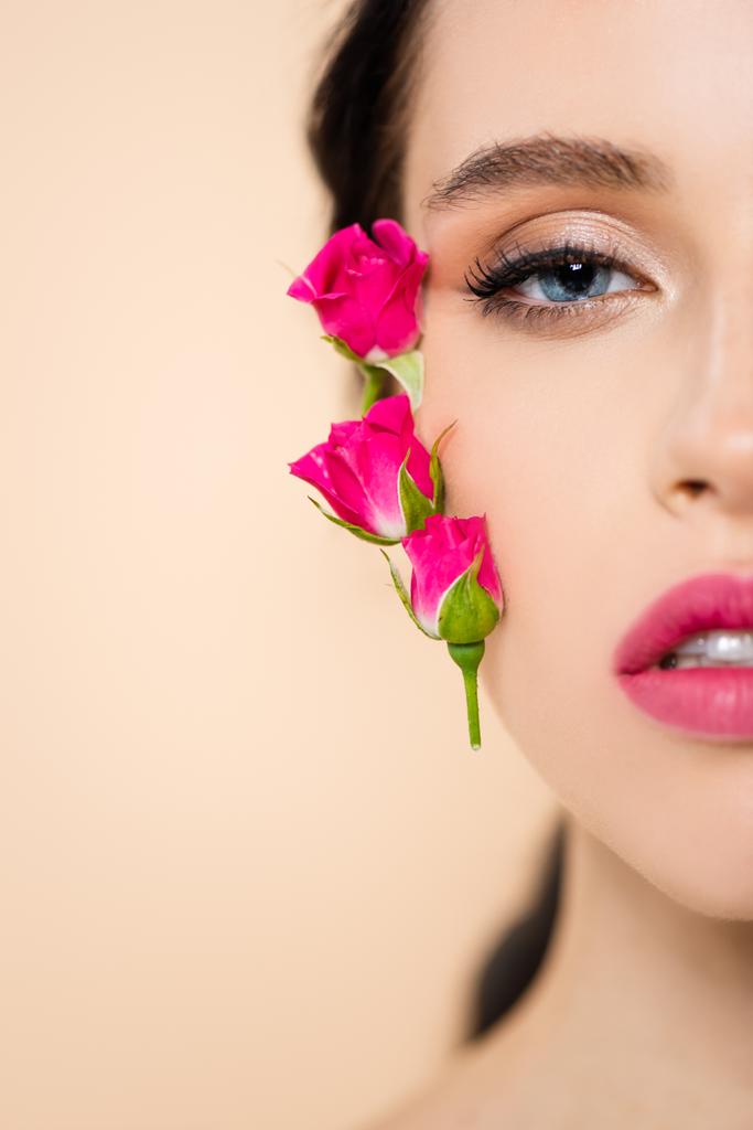oříznutý pohled na smyslnou mladou ženu s květinami na tváři při pohledu do kamery izolované na růžové  - Fotografie, Obrázek