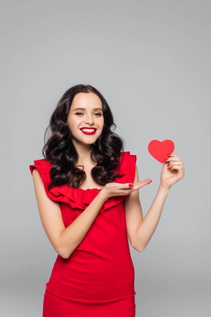 boldog fiatal nő mutató kézzel piros papír szív elszigetelt szürke - Fotó, kép