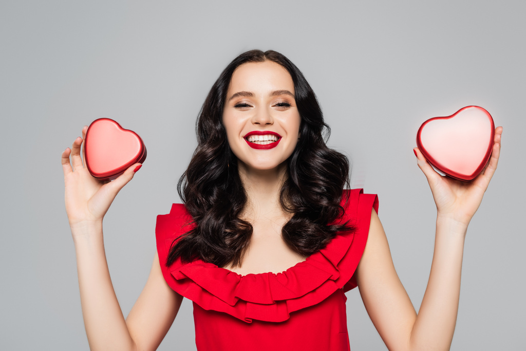 joyeuse jeune femme tenant des boîtes rouges en forme de coeur isolées sur gris - Photo, image
