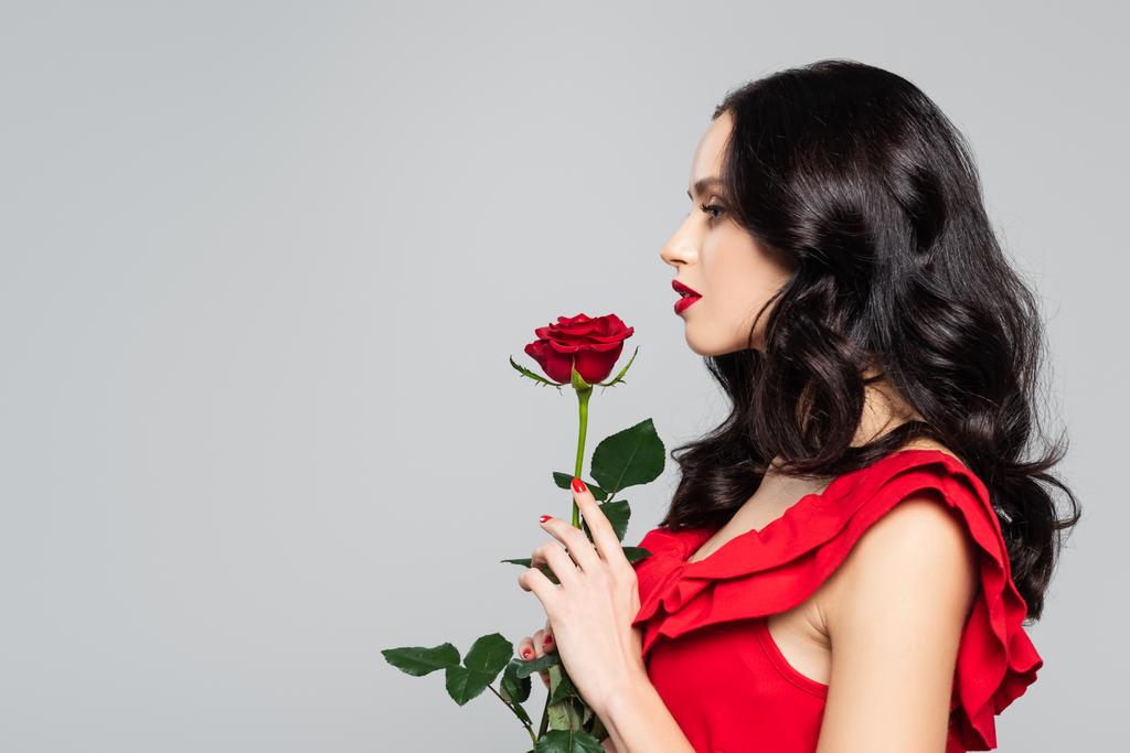 boční pohled na ženu držící červenou růži izolovanou na šedé - Fotografie, Obrázek