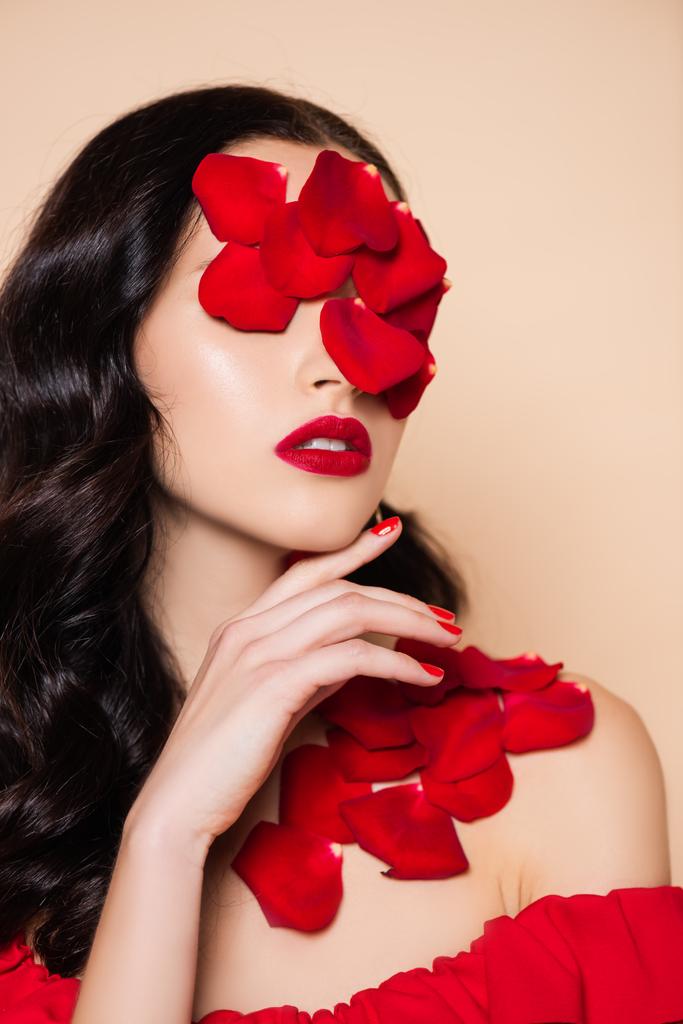 brunetka mladá žena s okvětními lístky červené růže na tváři izolované na růžové - Fotografie, Obrázek