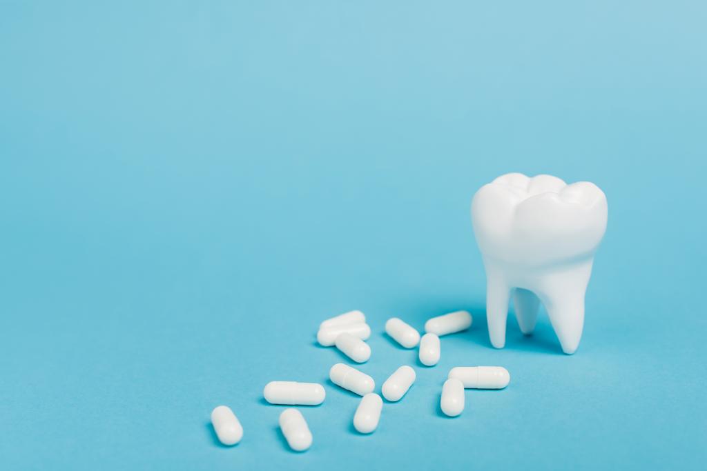 Крупный план белых таблеток и модели зубов на синем фоне - Фото, изображение