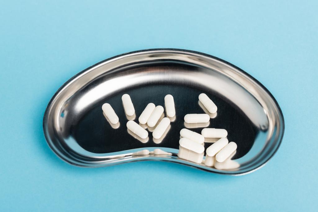 Vista de cerca de píldoras blancas en bandeja de metal sobre fondo azul - Foto, Imagen
