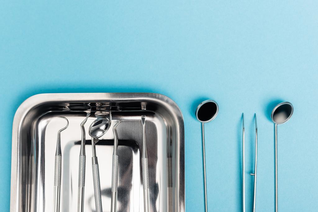 Draufsicht auf Reihe von Zahnwerkzeugen und Tablett auf blauem Hintergrund - Foto, Bild