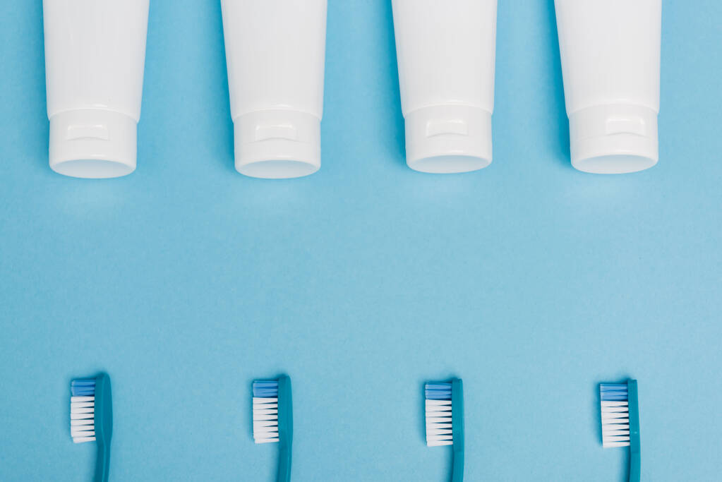 Vista superior de tubos con pasta de dientes y cepillos de dientes sobre fondo azul - Foto, imagen