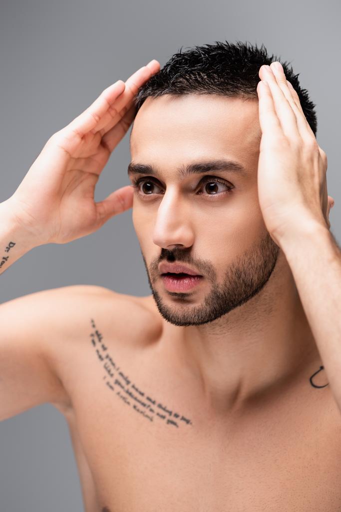 hemdloser, tätowierter hispanischer Mann, der Haare isoliert auf grau berührt - Foto, Bild