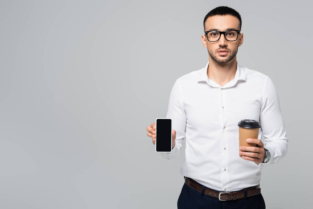 Genç İspanyol iş adamı elinde kahve tutuyor ve gri ekranda boş ekranlı akıllı telefon var. - Fotoğraf, Görsel