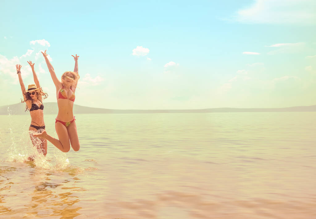 2 Mädchen springen hoch mit den Armen den spektakulären Sonnenaufgang an der Meeresküste hinauf.  - Foto, Bild
