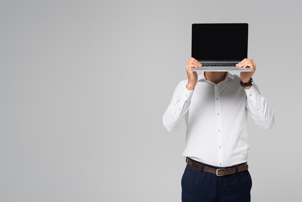 homem de negócios hispânico em camisa branca obscurecendo rosto com laptop isolado em cinza - Foto, Imagem