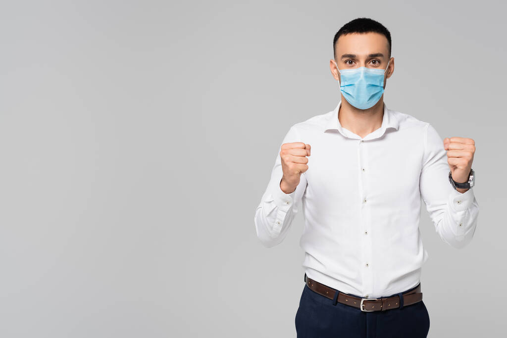 Erfolgreicher hispanischer Geschäftsmann in medizinischer Maske zeigt Siegergeste isoliert auf grau - Foto, Bild