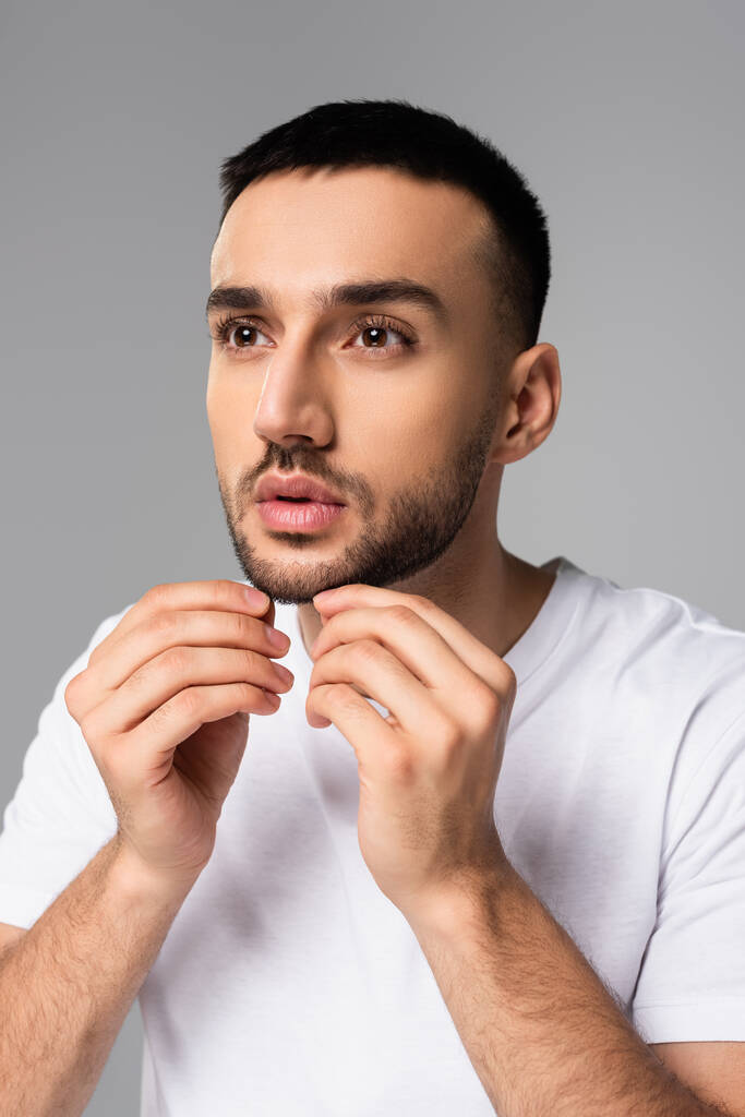 hombre hispano sin afeitar tocando cerdas en la cara aislado en gris - Foto, imagen