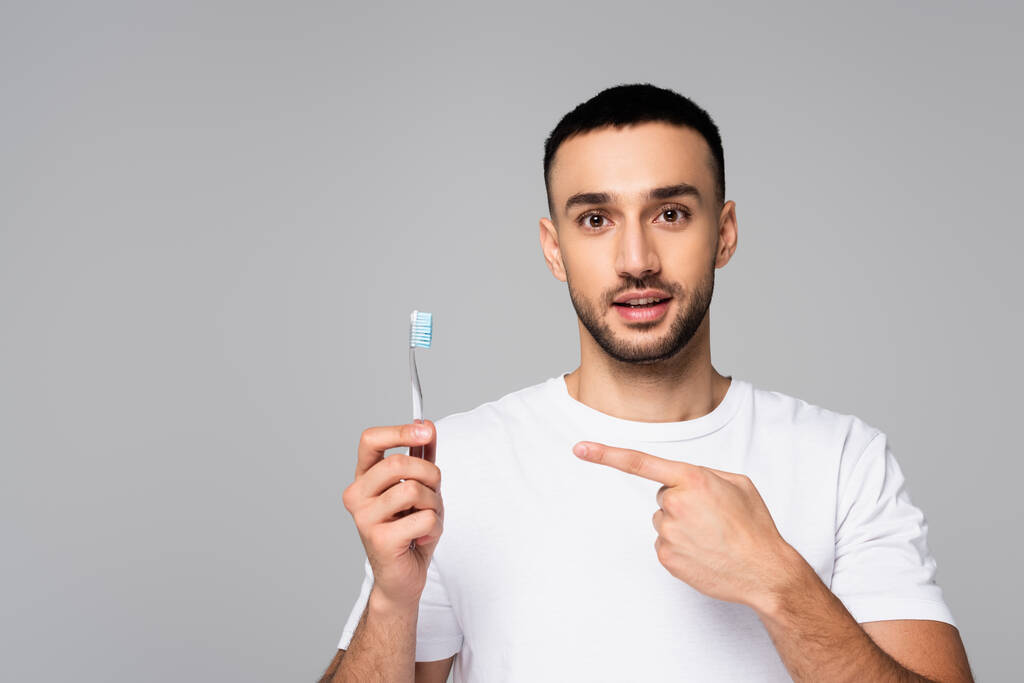 Esmer, İspanyol bir adam diş fırçasını işaret ediyor ve gri renkli kameraya bakıyor. - Fotoğraf, Görsel