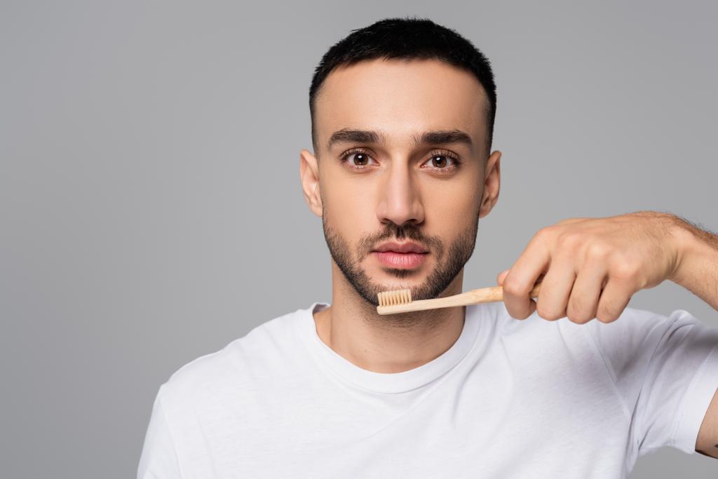 young hispanic man looking at camera while holding toothbrush isolated on grey - Photo, Image