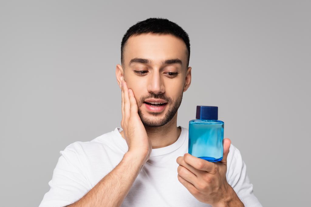 brünette hispanische Mann Anwendung Rasierwasser auf Gesicht isoliert auf grau - Foto, Bild