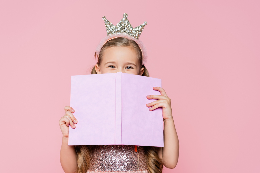 mała dziewczynka w koronie pokrycie twarzy z książki izolowane na różowy - Zdjęcie, obraz