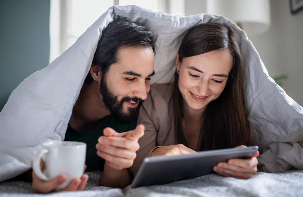 Młoda para zakochana używa tabletu na łóżku w domu. - Zdjęcie, obraz